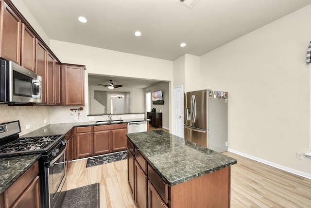 kitchen with dark stone counters, stainless steel appliances, ceiling fan, sink, and a center island