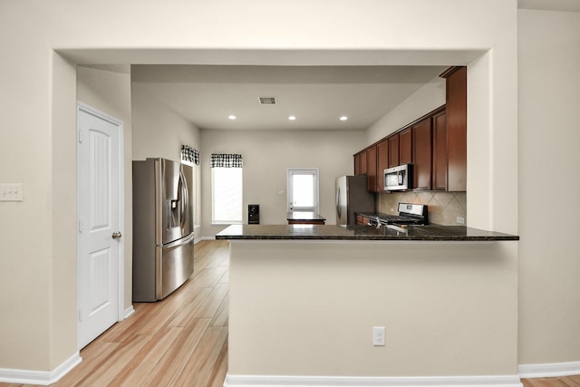 kitchen featuring backsplash, light hardwood / wood-style flooring, dark stone countertops, kitchen peninsula, and stainless steel appliances