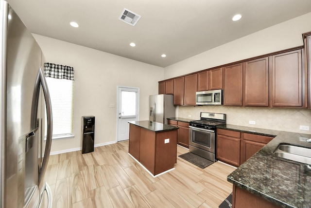 kitchen featuring sink, a center island, dark stone counters, and appliances with stainless steel finishes