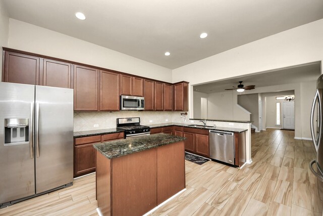 kitchen featuring sink, ceiling fan, dark stone countertops, a kitchen island, and stainless steel appliances