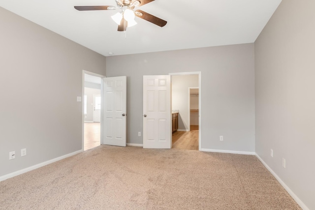 unfurnished bedroom with ceiling fan, a spacious closet, light carpet, and a closet