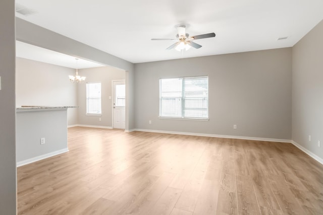 empty room featuring a healthy amount of sunlight, ceiling fan with notable chandelier, and light wood-type flooring