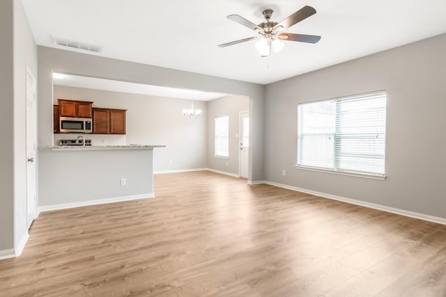 unfurnished living room featuring light hardwood / wood-style flooring and ceiling fan with notable chandelier