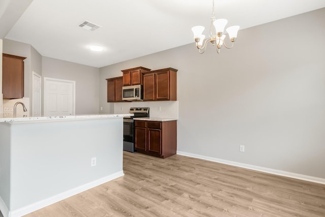 kitchen with light stone countertops, an inviting chandelier, light hardwood / wood-style flooring, decorative light fixtures, and appliances with stainless steel finishes