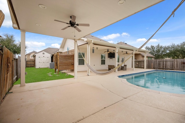 view of swimming pool featuring a storage shed, central air condition unit, ceiling fan, a patio, and a lawn