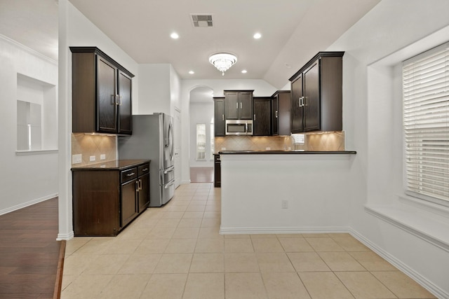 kitchen with dark brown cabinetry, decorative backsplash, light tile patterned floors, and stainless steel appliances