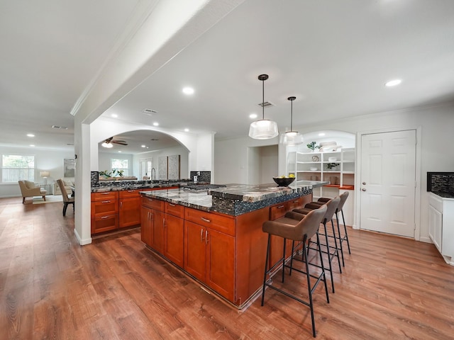 kitchen with crown molding, decorative light fixtures, hardwood / wood-style flooring, dark stone countertops, and a center island