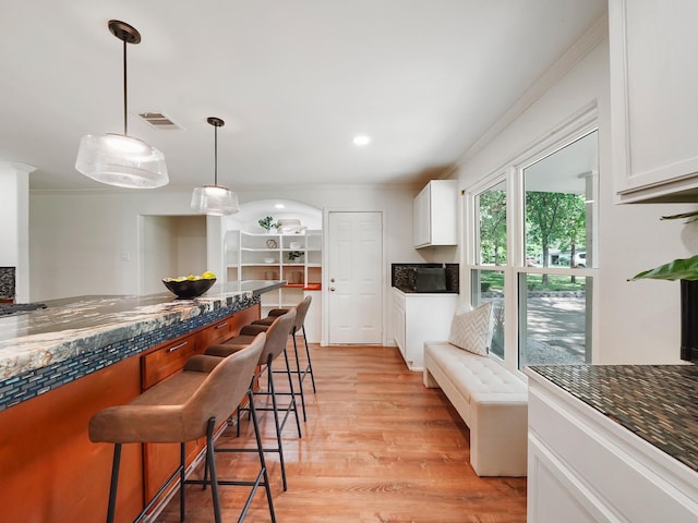 kitchen featuring pendant lighting, a kitchen breakfast bar, white cabinetry, and ornamental molding