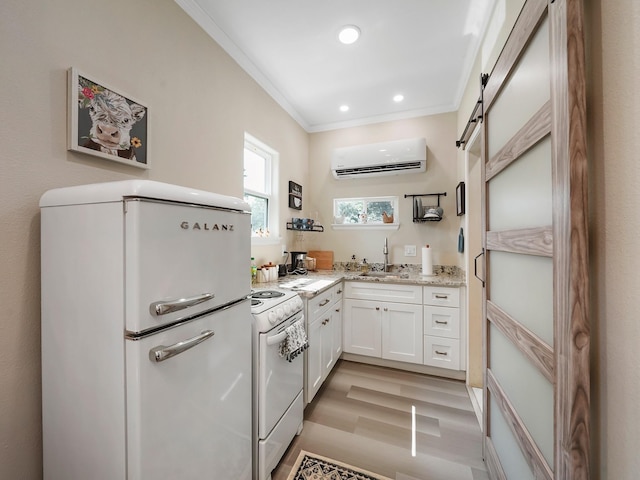 kitchen featuring white appliances, a wall unit AC, sink, a barn door, and white cabinetry