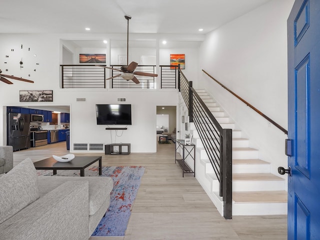 living room featuring a towering ceiling, light wood-type flooring, and ceiling fan