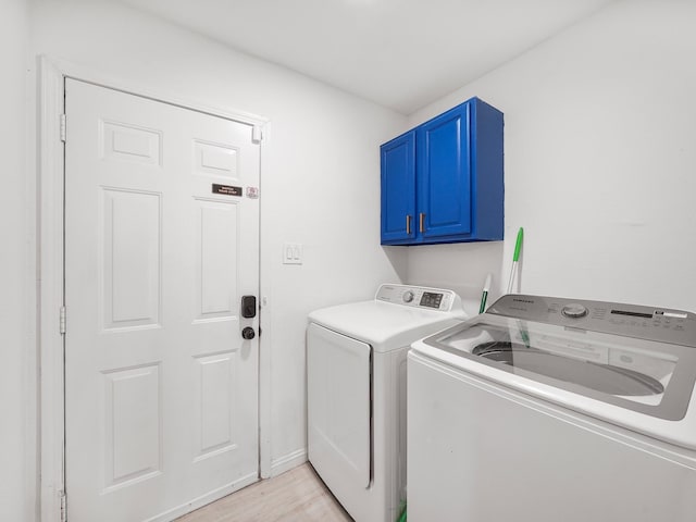 laundry room featuring washing machine and clothes dryer, light hardwood / wood-style flooring, and cabinets