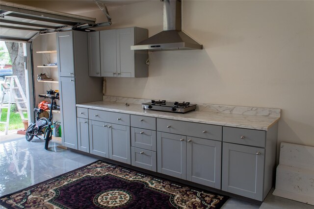 kitchen featuring gray cabinets, light stone counters, wall chimney range hood, and stainless steel gas cooktop