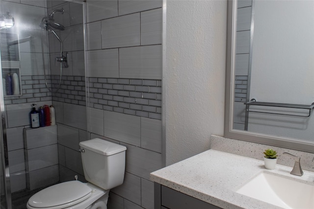 bathroom featuring toilet, a tile shower, and vanity