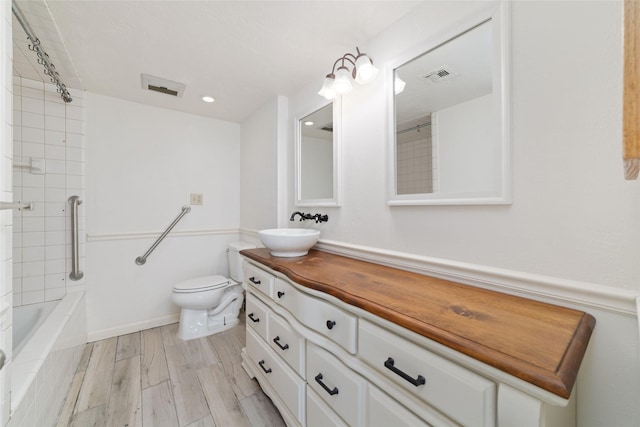 full bathroom with vanity, hardwood / wood-style flooring, toilet, and tiled shower / bath