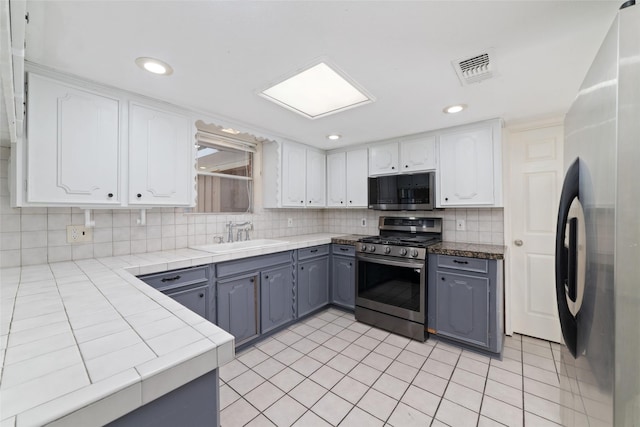 kitchen featuring decorative backsplash, stainless steel appliances, sink, white cabinets, and gray cabinets