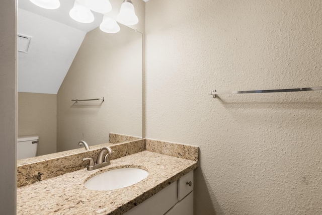 bathroom with toilet, vanity, and vaulted ceiling