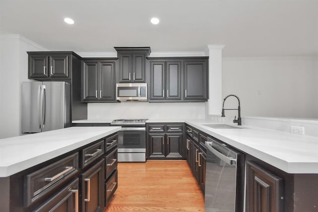 kitchen with crown molding, sink, light wood-type flooring, kitchen peninsula, and stainless steel appliances