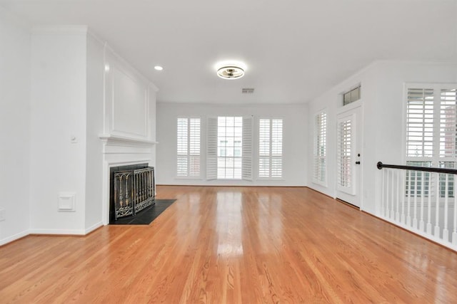 unfurnished living room featuring light wood finished floors, visible vents, a wealth of natural light, and a fireplace with flush hearth