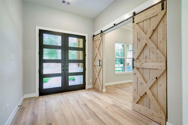 foyer entrance featuring french doors, a barn door, and light hardwood / wood-style flooring