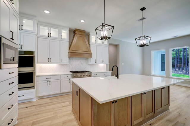 kitchen featuring white cabinets, custom exhaust hood, a kitchen island with sink, and stainless steel appliances