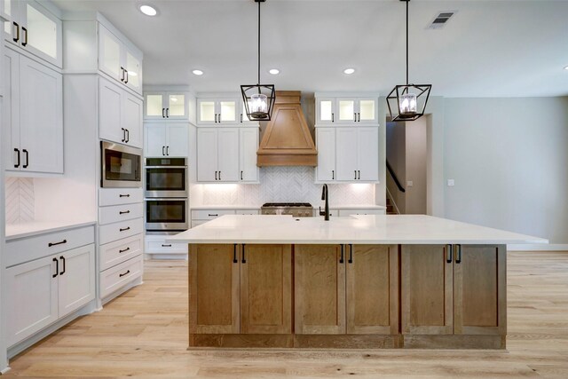 kitchen featuring stainless steel appliances, white cabinetry, custom range hood, and a spacious island