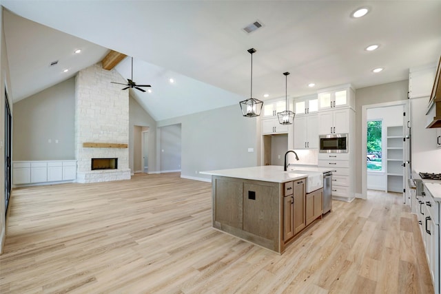 kitchen featuring a stone fireplace, a center island with sink, light hardwood / wood-style floors, stainless steel appliances, and white cabinets