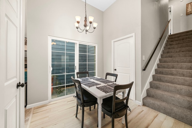 dining area with an inviting chandelier, a towering ceiling, and light wood-type flooring