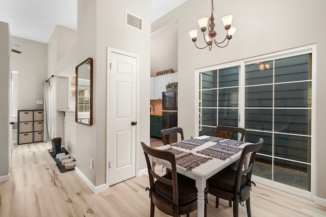 dining room featuring a towering ceiling, a chandelier, and light hardwood / wood-style flooring