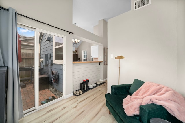 living area with an inviting chandelier, vaulted ceiling, and light wood-type flooring