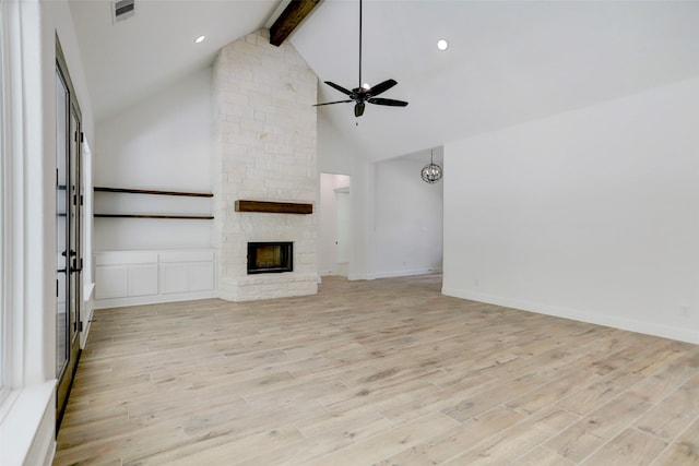 unfurnished living room with beam ceiling, ceiling fan, a stone fireplace, high vaulted ceiling, and light hardwood / wood-style floors