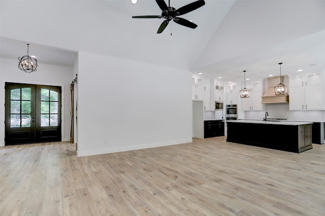 unfurnished living room featuring high vaulted ceiling, french doors, sink, light hardwood / wood-style flooring, and ceiling fan