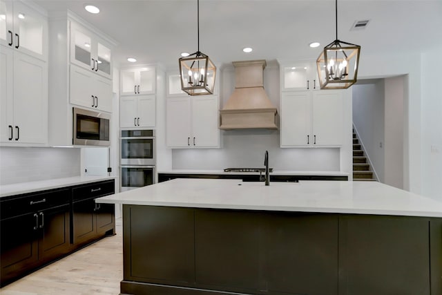 kitchen with pendant lighting, white cabinets, an island with sink, appliances with stainless steel finishes, and custom range hood