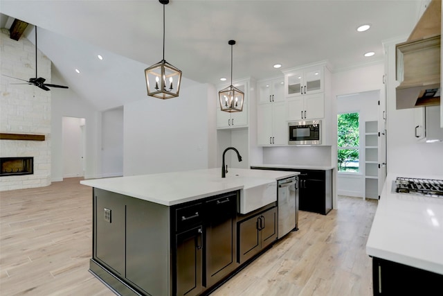 kitchen with stainless steel appliances, sink, a center island with sink, white cabinets, and a stone fireplace