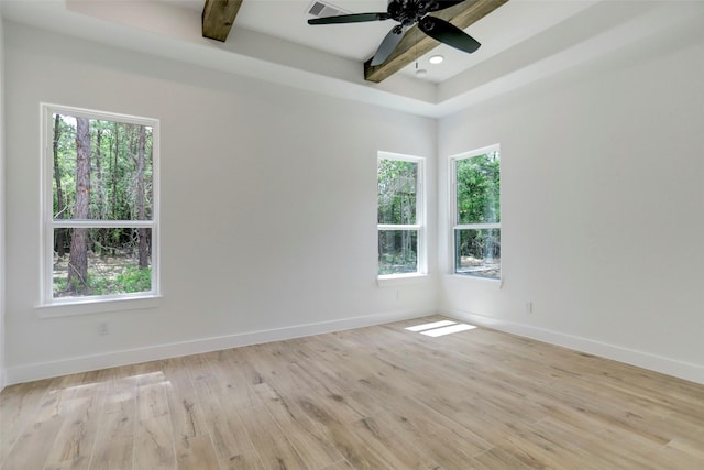 spare room with a tray ceiling, a wealth of natural light, ceiling fan, and light wood-type flooring