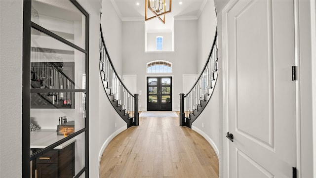 entryway with french doors, light wood-type flooring, a high ceiling, and ornamental molding