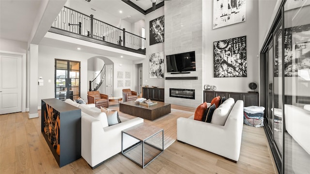 living room with a high ceiling, a tile fireplace, and light hardwood / wood-style flooring