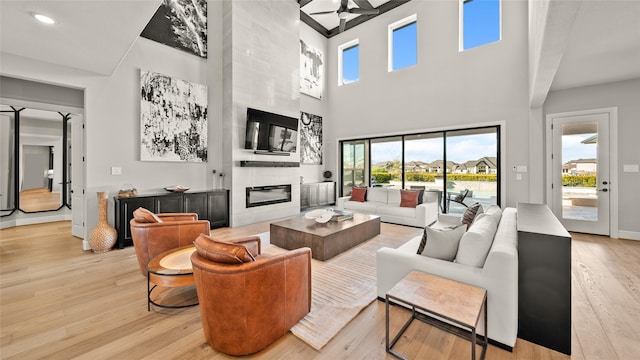 living room featuring ceiling fan, a large fireplace, a towering ceiling, and light hardwood / wood-style flooring