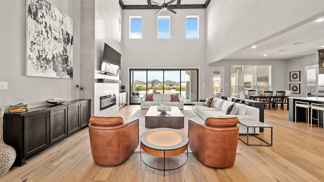 living room featuring a fireplace, a high ceiling, light wood-type flooring, and ceiling fan