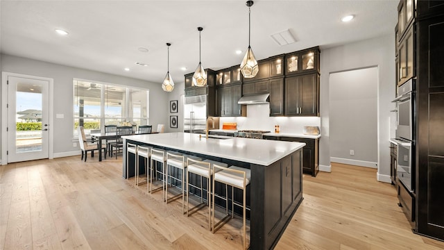 kitchen featuring sink, an island with sink, decorative light fixtures, dark brown cabinetry, and stainless steel appliances