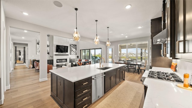 kitchen featuring ventilation hood, sink, stainless steel dishwasher, a fireplace, and decorative light fixtures