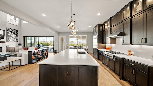 kitchen featuring a kitchen island with sink, sink, decorative light fixtures, light hardwood / wood-style floors, and stainless steel appliances