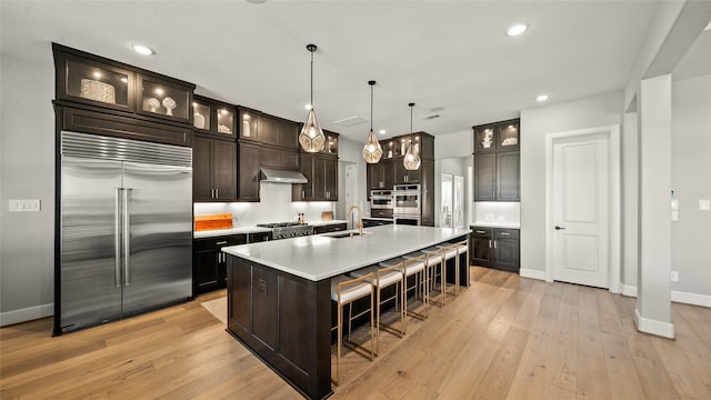 kitchen featuring a kitchen island with sink, hanging light fixtures, sink, appliances with stainless steel finishes, and dark brown cabinetry