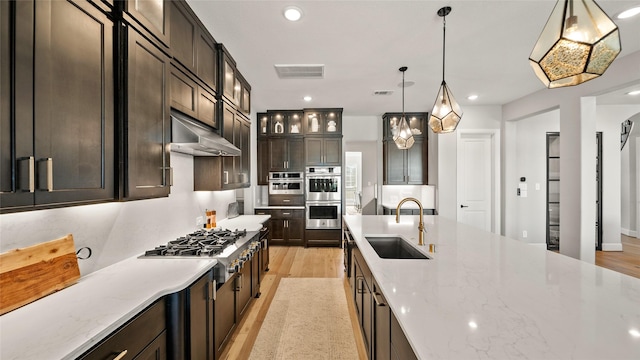 kitchen with pendant lighting, sink, light hardwood / wood-style flooring, light stone countertops, and appliances with stainless steel finishes