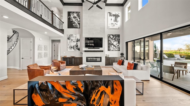 living room with ceiling fan, light wood-type flooring, a fireplace, and a towering ceiling