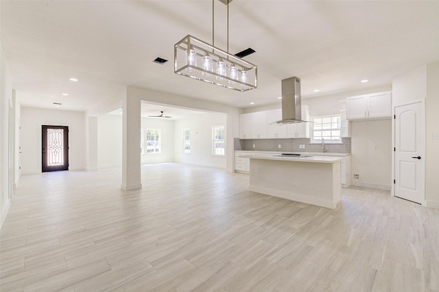 kitchen with a kitchen island, white cabinetry, open floor plan, light countertops, and island exhaust hood