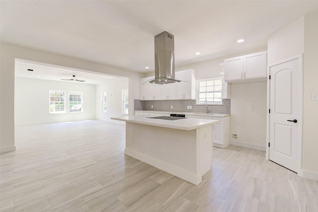 kitchen featuring white cabinetry, island range hood, light countertops, and a sink