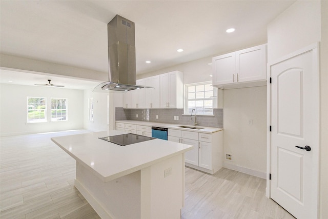 kitchen featuring island exhaust hood, black electric stovetop, light countertops, white cabinets, and a sink