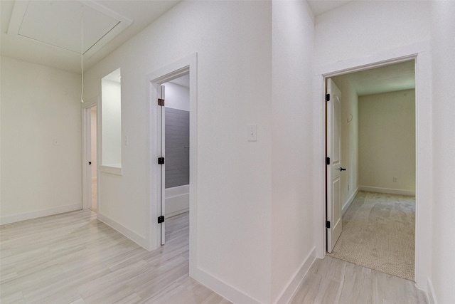 hallway with attic access, light wood-style floors, and baseboards