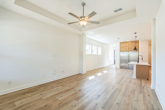 unfurnished living room with ceiling fan, light hardwood / wood-style floors, a tray ceiling, and sink