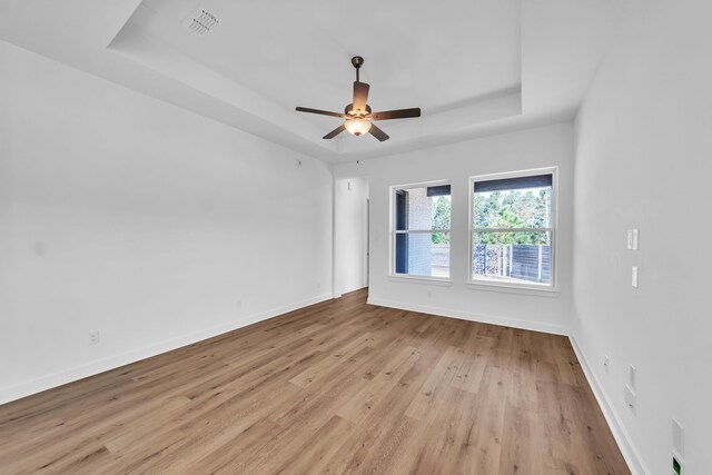 spare room featuring light hardwood / wood-style flooring, ceiling fan, and a raised ceiling